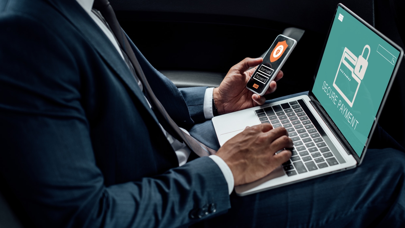 cropped view of african american businessman using laptop and smartphone in car with cyber security